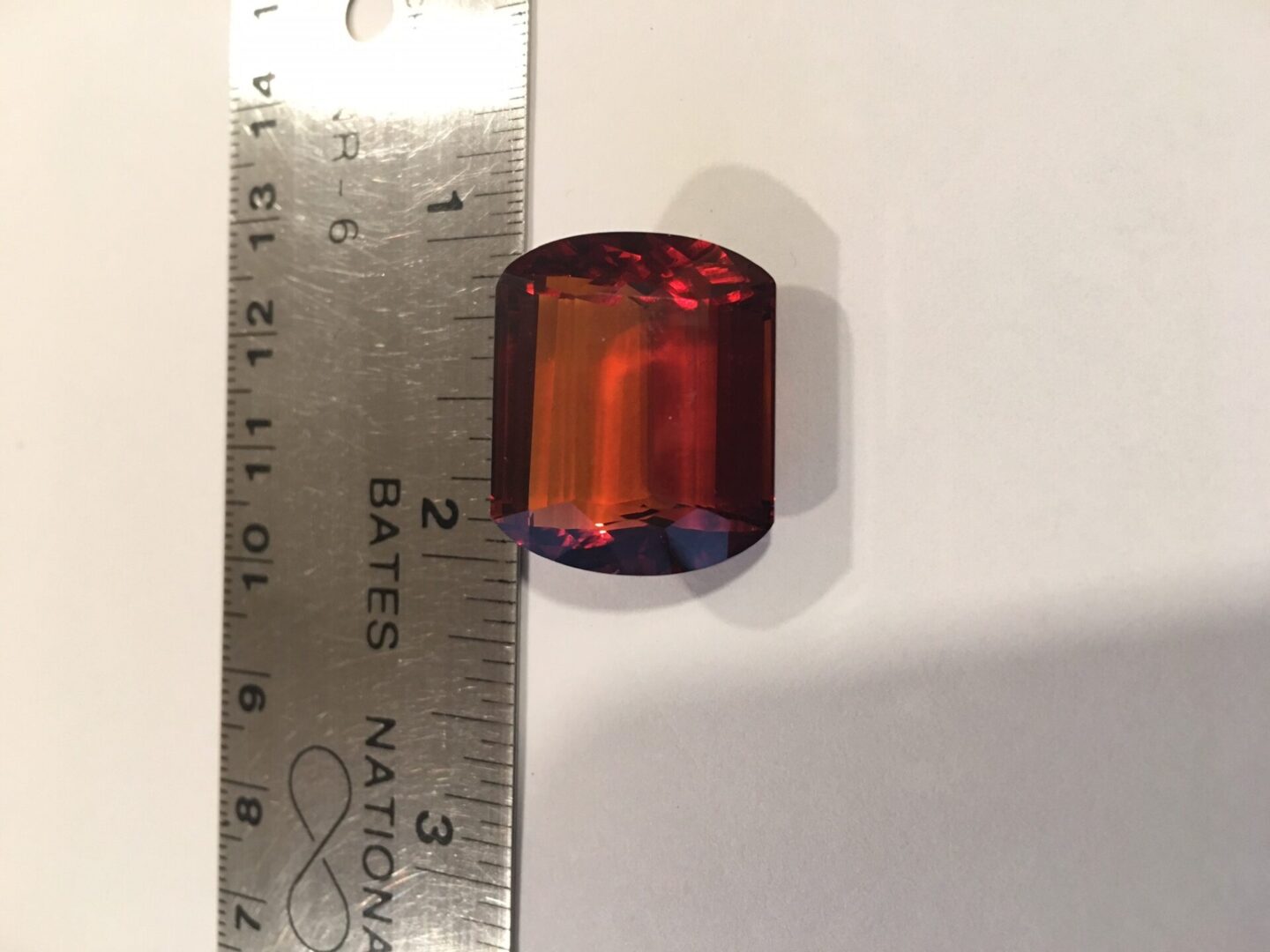 A red and blue glass bead is next to a ruler.