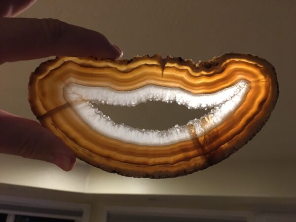 A person holding an agate slice with a smile on it.