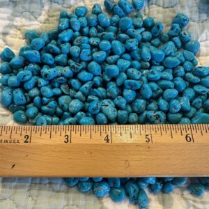 Turquoise beads and 50 Grams of Coral on a bed with a ruler next to them.