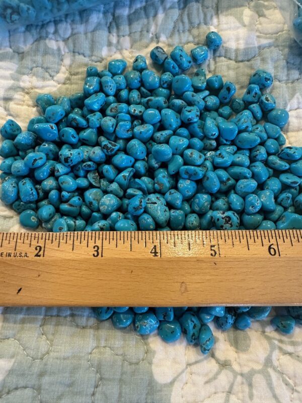 Turquoise beads and 50 Grams of Coral on a bed with a ruler next to them.